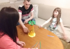 dziewczynka w pofalowanych włosach gra z rodzicami przy małym stoliku