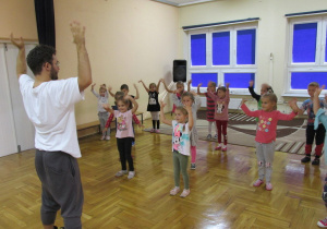 dzieci tańczą z instruktorem z rękami uniesionymi po bokach