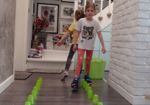 dziewczyny chodzą między zielonymi kubkami rozstawionymi na podłodze w rządkach
