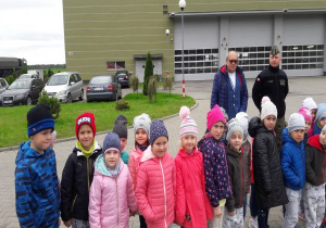 dzieci stoją przed hangarem straży pożarnej z przewodnikiem i wojskowym