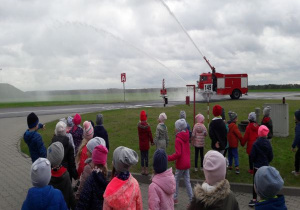 dzieci obserwują armatki wodne podczas pracy zamontowane na wozie strażackim