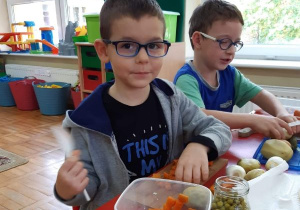 chłopiec kroi marchewkę i wrzuca do pojemnika