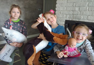trzy dziewczynki ze swoimi maskotkami: dmuchanym białym kotem, dużym brązowo - czarnym psem, maskotką oraz małą lalką