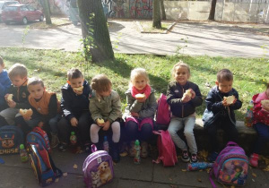 dzieci siedzą na dworze, na murku i jedzą bułki z serem