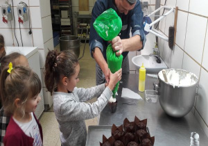 tata pomaga dziewczynce ozdabić mufinkę bitą śmietaną
