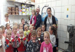 tata trzyma córkę, obok stoi nauczycielka a dzieci trzymają mufinki