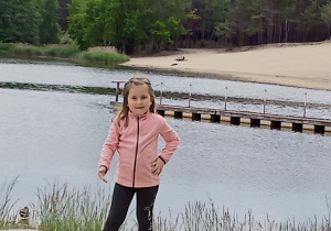 dziewczynka w ubraniu stoi na plaży nad wodą w pobliżu lasu