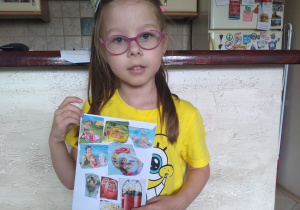 dziewczynka stoi i trzyma swoja pracę: na kartce naklejone są obrazki: basen dla dzieci, rękawki do pływania, koło do pływania, lody i pop corn.