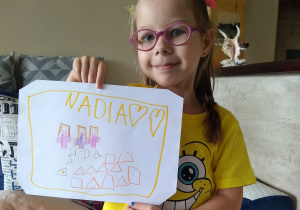 dziewczynka trzyma kartkę z napisem Nadia i narysowanymi 3 koleżankami i klockami
