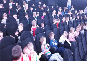 dzieci siedzą na fotelach w planetarium