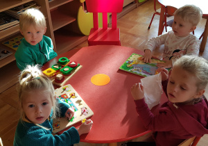 maluszki bawią się przy stoliku drewnianymi układankami