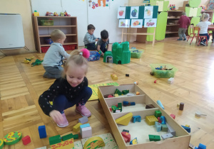 maluszki bawia sie na podłodze drewnianymi klockami i plastikową górą z dinozaurami