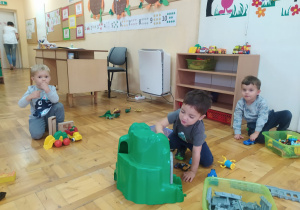 w sali chłopcy bawią się na podłodze zabawkami obok biurka nauczycielki