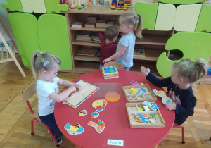 maluszki przy okrągłym, czerwonym stoliku układają drewniane, kolorowe puzzle