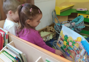 dziewczynka z chłopcem oglądają książkę siedząc na ławce w kąciku dom
