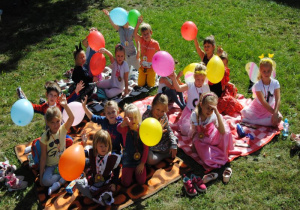 dzieci z gr. VI z żółtymi balonami siedzą na kocu w ogrodzie