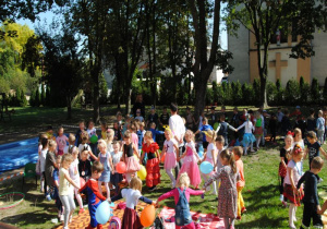 wszystkie dzieci tańczą w grupowych kołach, trzymając balony i śpiewają piosenkę