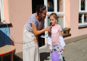 na tarasie dziewczynka z fioletowym balonem mówi do mikrofonu, który trzyma nauczycielka