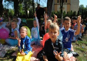 dzieci siedzą w ogrodzie i pokazują palce