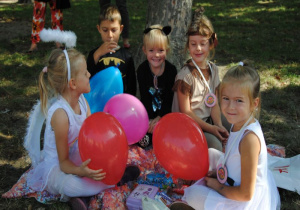 wesołe dzieci z balonami siedzą na kocu pod drzewem