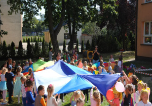 w ogrodzie dzieci bawia się chustami animacyjnymi w trzech grupach