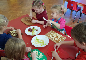 dzieci kroja banany. winogrono i jabłka na sałatkę owocową