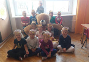 dzieci z grupy dzieci z grupy V z opaskami z misiem na głowie pozują z dużą maskotka misia z umalowanymi twarzami pozują z dużą maskotka misia