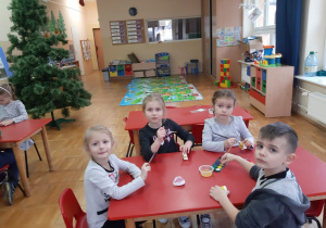 dzieci przy stolikach malują farbami ozdoby na choinkę