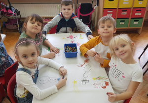 dzieci przy stoliku pokazują rysunki na świątecznym obrusie