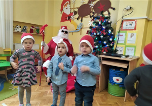 dzieci stoją i śpiewają Mikołajowi piosenkę i ilustrują ruchem