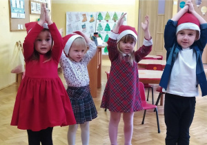 dzieci w czerwonych czapkach stoją z rękami w górze - "czapeczka" i śpiewają