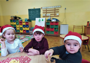 dzieci siedzą przy stoliku i jedzą paluszki