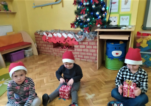 dzieci siedzą i rozpakowują prezenty