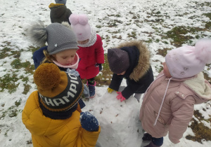 dzieci dolepiają śnieg do kuli śniężnej