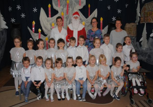 zdjęcie grupowe dzieci z gr8 w biało - srebrnych strojach z Mikołajem, opiekunką i nauczycielkami