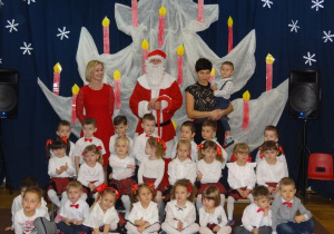 zdjęcie grupowe dzieci z gr9 w czerwono - białych strojach z Mikołajem i nauczycielkami