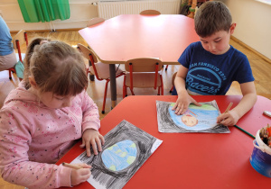 dzieci siedzą przy stoliku i rysują kredkami prace o Ziemi
