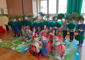 dzieci z gr III pozują do zdjęcia, chłopcy stoją z opaskami na głowie - trawami a dziewczynki siedzą przed nimi z akcesoriami biedronek i motyli