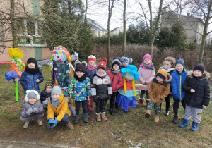 dzieci z grupy IX stoją przed przedszkolem i pokazują 3 Marzanny