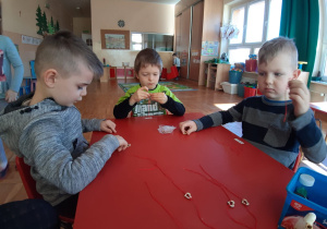 chłopcy przy stoliku montują serduszko na czerwonym sznurku