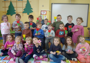 dzieci z grupy VIII - dziewczynki z kwiatkami wykonanymi z lizaka a chłopcy z kwiatkami zrobionymi z rolki papieru (łodyga) oraz kolorowego kielicha tulipana zamocowanego na rolce