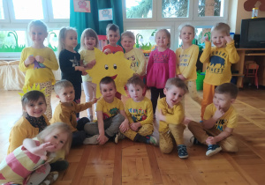dzieci z grupy II pokazują ukończoną swoją pracę grupową - kontur dużego żółtego słońca wyklejonego kawałkami żółtego papieru