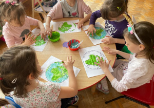 dzieci przy stolikach malują kontur Ziemi palcem i farbami: zieloną i niebieską