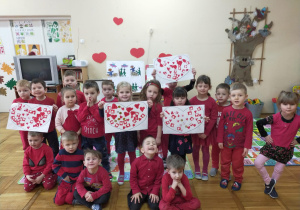 dzieci w czerwonych ubraniach z grupy IX z pracami plastycznymi - duże serduszka wyklejone małymi czerwonymi serduszkami