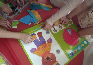 dzieci na tablicy magnetycznej z misiem naklejają elementy związane z porą rokuu