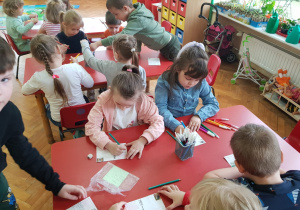 dzieci przy stolikach piszą pozdrowienia i ozdabiają swoje kartki