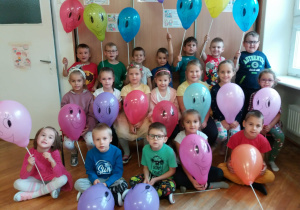 dzieci z grupy V pozują do zdjęcia z kolorowymi balonami i narysowanymi uśmiechniętymi buziami