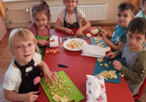 dzieci na deskach kroją owoce i wrzucają do miski na środku stolika