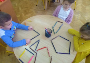 dzieci przy stoliku układają wzory z kolorowych kredek
