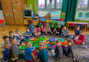 dzieci siedzą w kole wokół kolorowych pojemników wypełnionych kolorowymi ziarnami ryżu